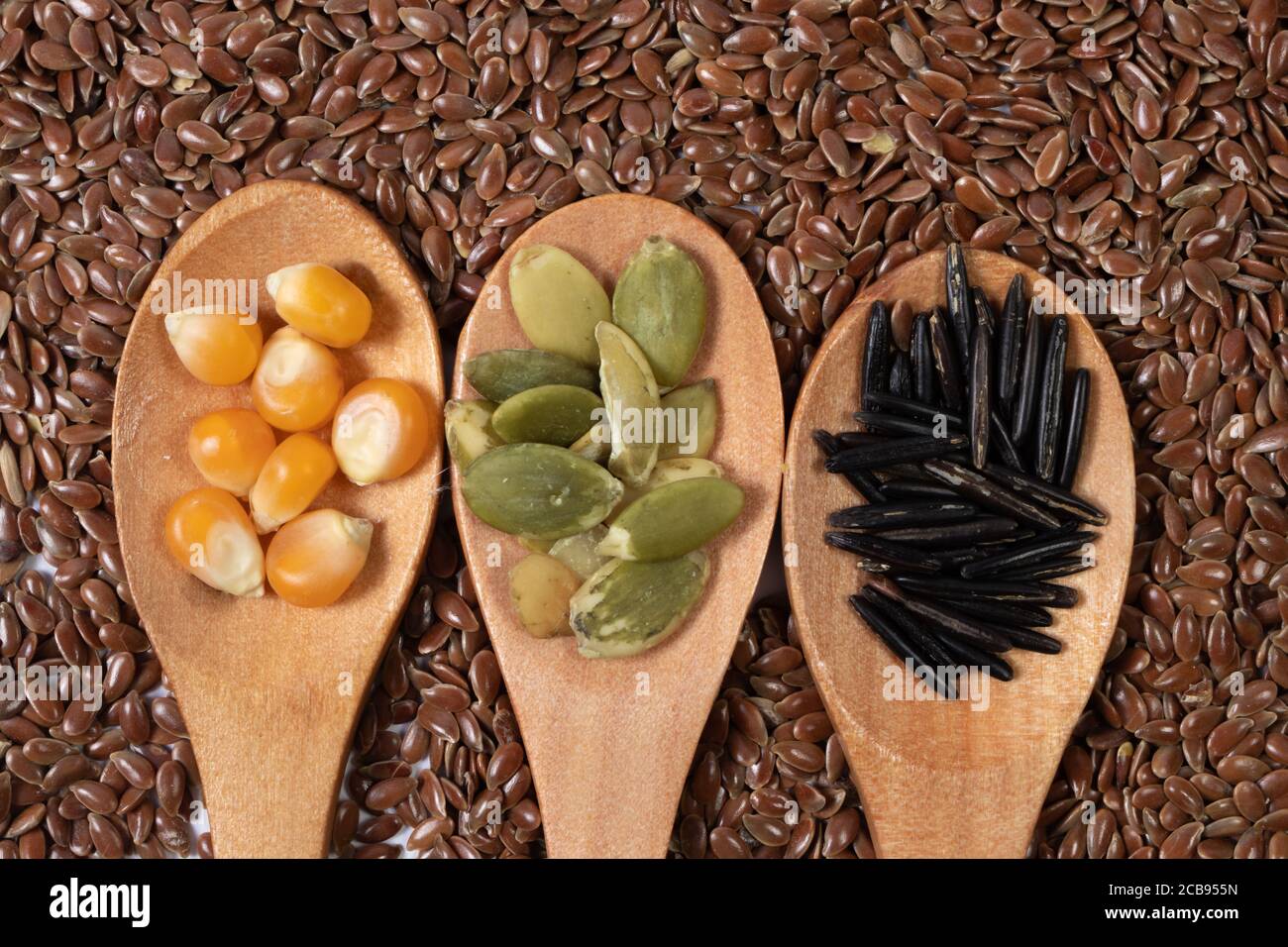 Verschiedene Samen -Mais, Kürbis, Kaffee- in Holzlöffeln auf einer Oberfläche von Samen und braunen Hintergrund Stockfoto