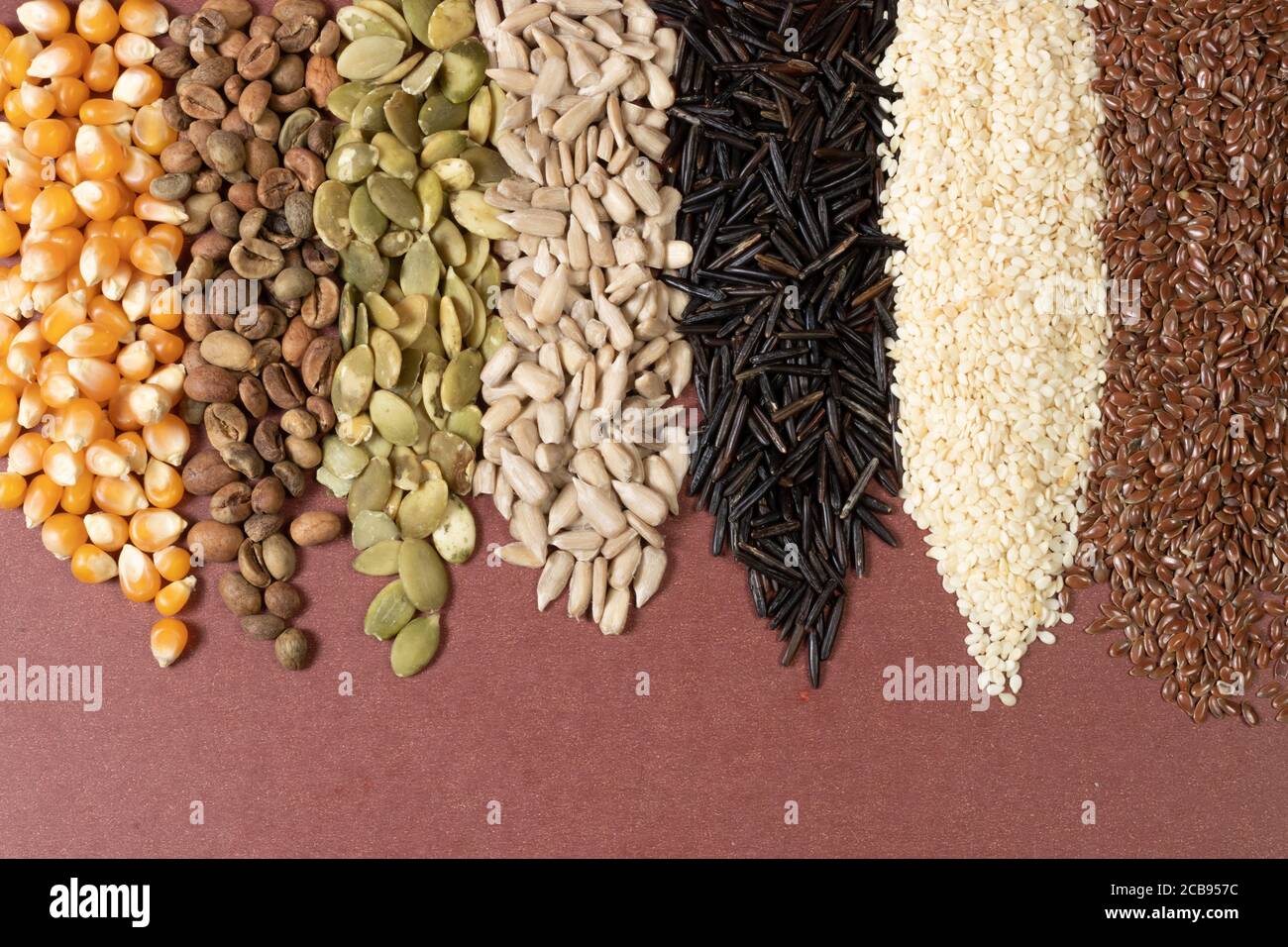 Verschiedene Getreide und Samen - Mais, Kürbis, Kaffee, Quinoa, Pfeffer, Reis, Hirse Sonnenblume - auf einer braunen Oberfläche Stockfoto