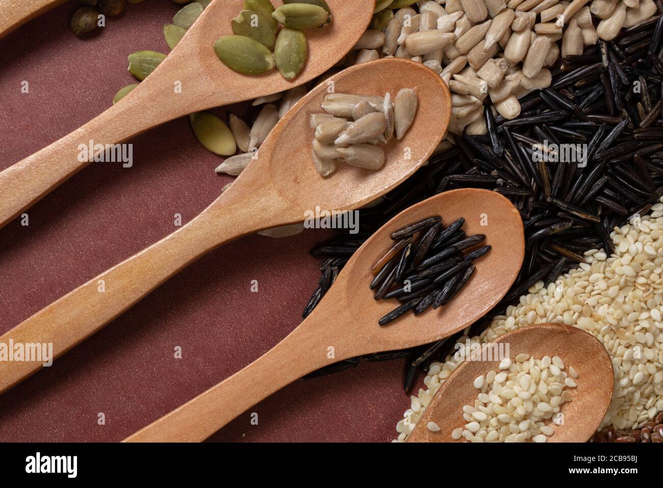 Verschiedene Samen -Quinoa, Kürbis, Kaffee, Pfeffer, Reis, Sonnenblumen- in Holzlöffeln auf einer Oberfläche von verschiedenen Samen und braunen Hintergrund Stockfoto