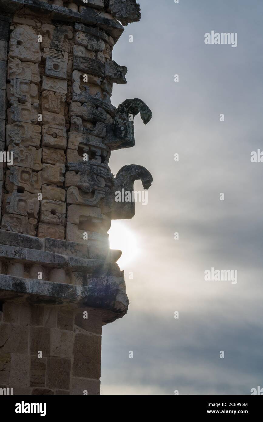 Die Sonne hinter den geschnitzten Stein Chaac Masken mit ihren Curling Nasen an der Ecke des Nordgebäudes von Das Nunnery Quadrangle im vorspanischen Stockfoto