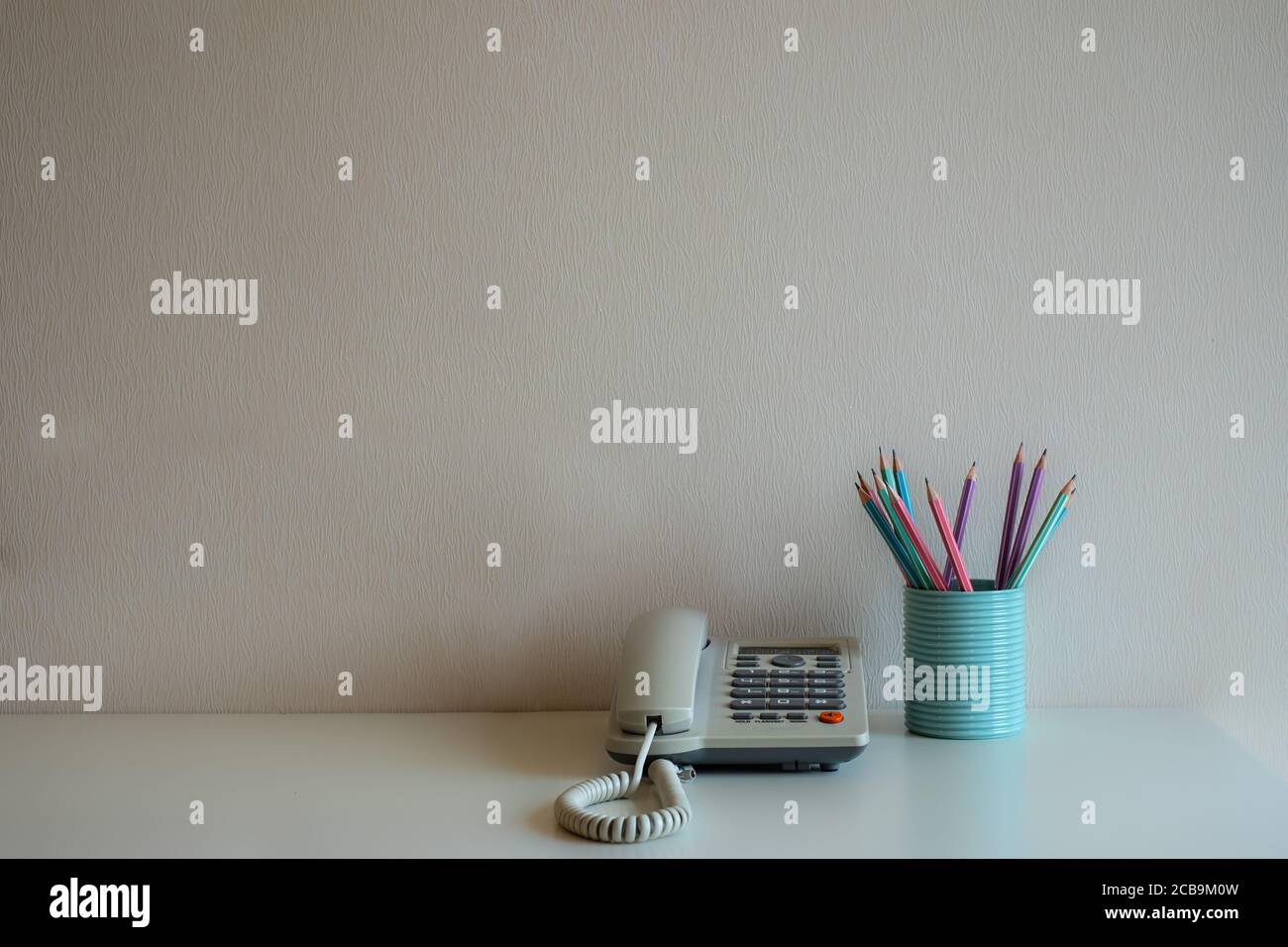 Telefon und Pastellstifte im blauen Glas auf dem Schreibtisch mit grauem Wandhintergrund Stockfoto