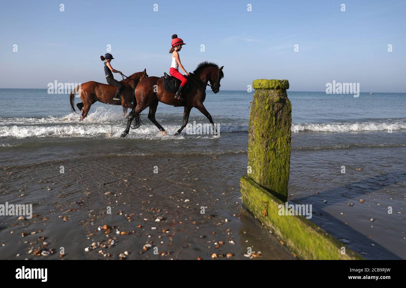 Zwei Reiter kühlen ihre Pferde im Meer bei East Wittering in West Sussex ab. Stockfoto