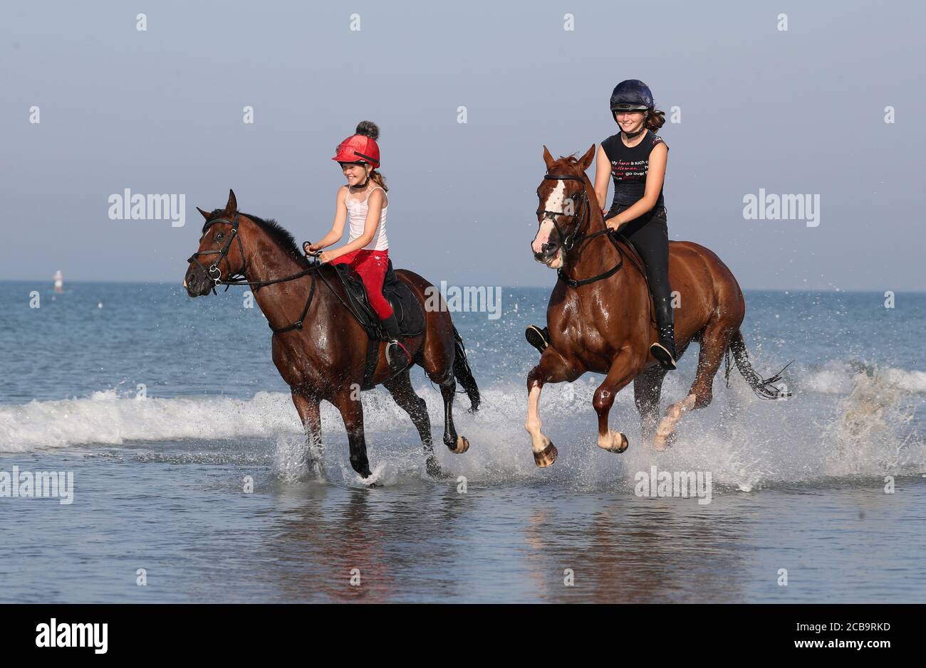 Zwei Reiter kühlen ihre Pferde im Meer bei East Wittering in West Sussex ab. Stockfoto