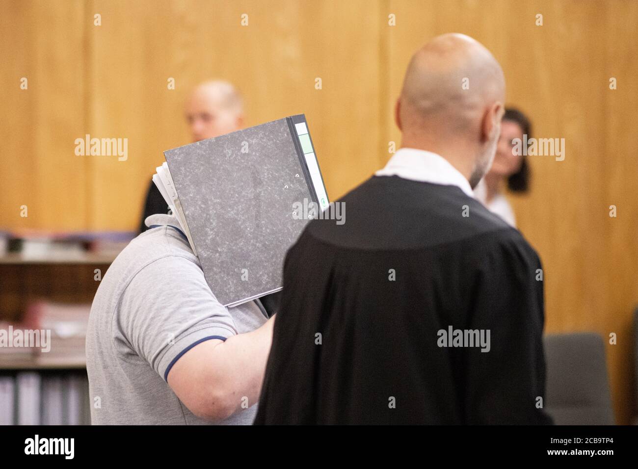 Essen, Deutschland. August 2020. Der Angeklagte (l) betritt zu Beginn des Prozesses den Gerichtssaal mit einem Aktenordner vor seinem Gesicht. Der 47-jährige Krefelder soll im Juni 2019 einen Bekannten erstickt haben, als ihr eine Plastiktüte über den Kopf gezogen wurde. Hintergrund des Verbrechens soll Eifersucht gewesen sein. Die Frau wollte angeblich mit ihm brechen. Der Körper wurde noch nicht gefunden. Quelle: Marcel Kusch/dpa/Alamy Live News Stockfoto