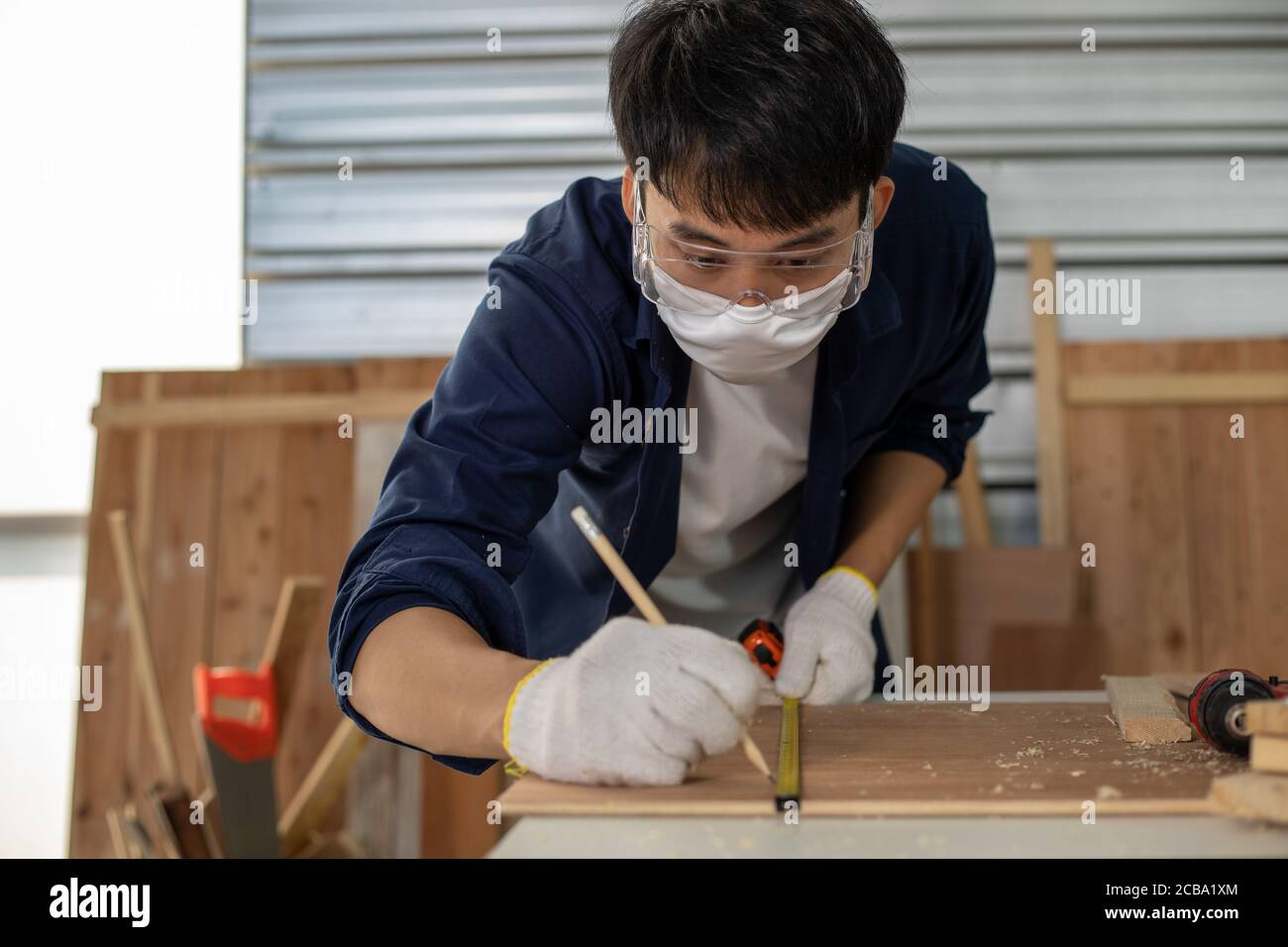 Asian man Carpenter arbeitet mit technischem Zeichnen oder Baupapier, das auf einer Werkstatt mit Zimmermannswerkzeugen und Holz zu Hause liegt Stockfoto