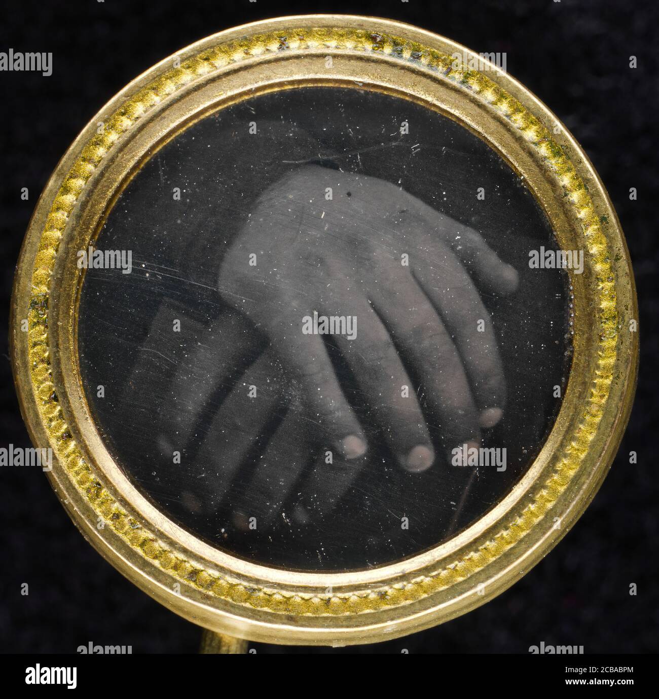 Knopf, 1840er-50s. Zwei Hände, die auf einem Buch ruhen und in einen zweiteiligen goldgewaschenen Messingrahmen mit einer Schlaufe auf der Rückseite zum Nähen an einem Kleidungsstück eingegliedert sind. Der Knopf wurde in den frühen 1980er Jahren auf einem Flohmarkt in Massachusetts entdeckt. Die Verwendung von Tasten für politische Zwecke in den Vereinigten Staaten begann in den 1700er Jahren. Viele Jahre lang wurde angenommen, dass das Bild ein Anti-Sklaverei-Motiv von zwei Händen - eine schwarze, eine weiße - auf einer Bibel ruhend darstellt. Heute, nach detaillierter digitaler Bildgebung, scheint das Foto die Hände nur eines Individuums zu zeigen. Die symbolische Bedeutung dieses einzigartigen Buttons ist somit offen für Stockfoto