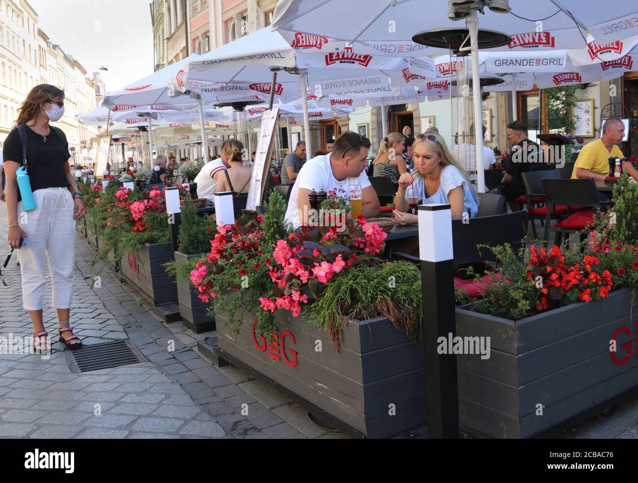 Krakau. Krakau. Polen. Hauptmarkt, Touristen in einem Restaurant Sommergarten. Ein maskiertes Mädchen, das zusieht. Stockfoto