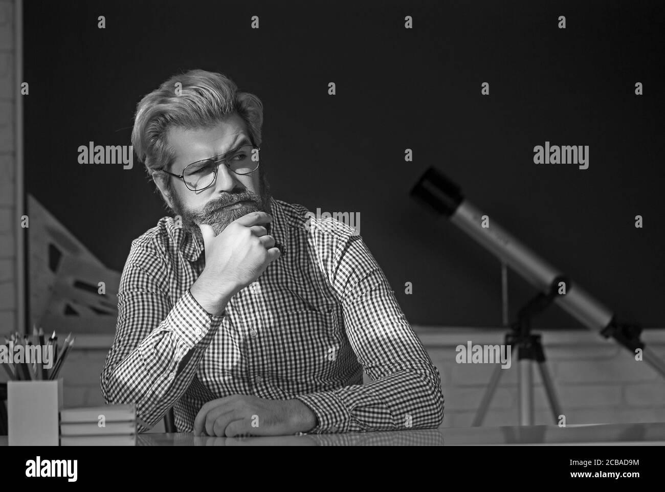 Junger männlicher Lehrer mit Büchern, die im Klassenzimmer am Tisch sitzen. Stockfoto