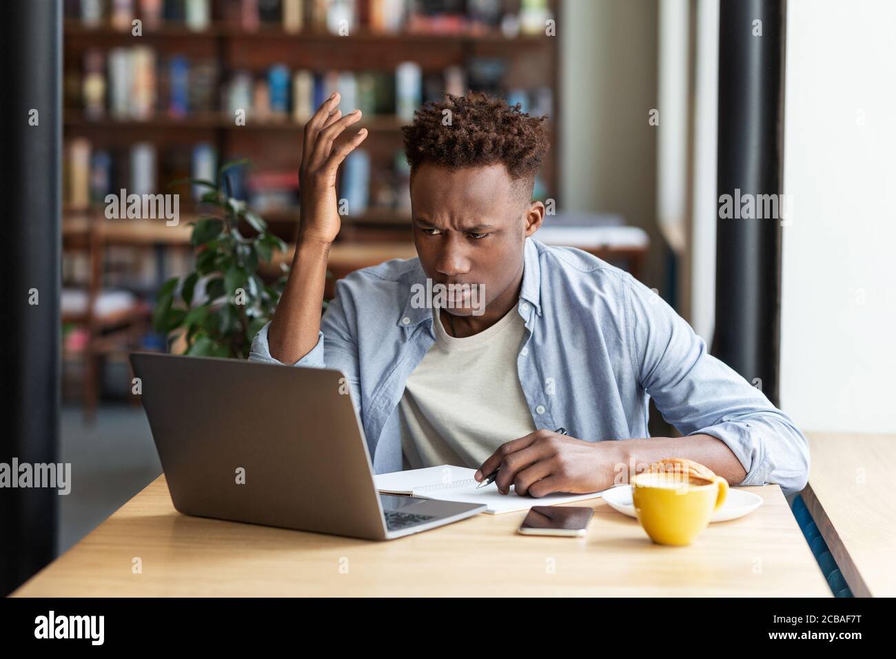 Irritiert afroamerikanischen Kerl mit Laptop, um auf schwer zu arbeiten Business-Projekt in der Stadt Café Stockfoto