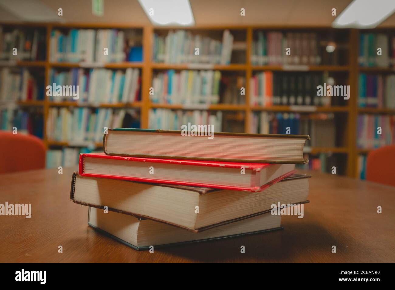 Stapel von Büchern auf dem Tisch und verschwommenes Bücherregal im Bibliotheksraum, Bildungshintergrund. Stockfoto
