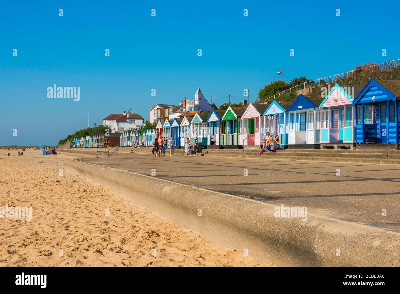 Suffolk Coast UK, Blick im Sommer auf die Menschen sitzen vor bunten Strandhütten entlang der Küste in Southwold an der Suffolk Küste, England, Großbritannien Stockfoto