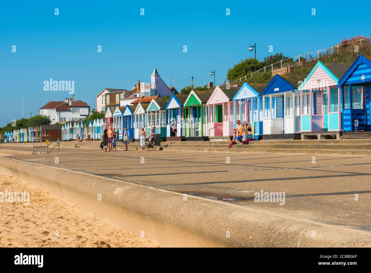 Suffolk Seaside, Blick im Sommer auf die Menschen sitzen vor ihren bunten Strandhütten entlang der Küste in Southwold an der Suffolk Küste, England, Großbritannien Stockfoto