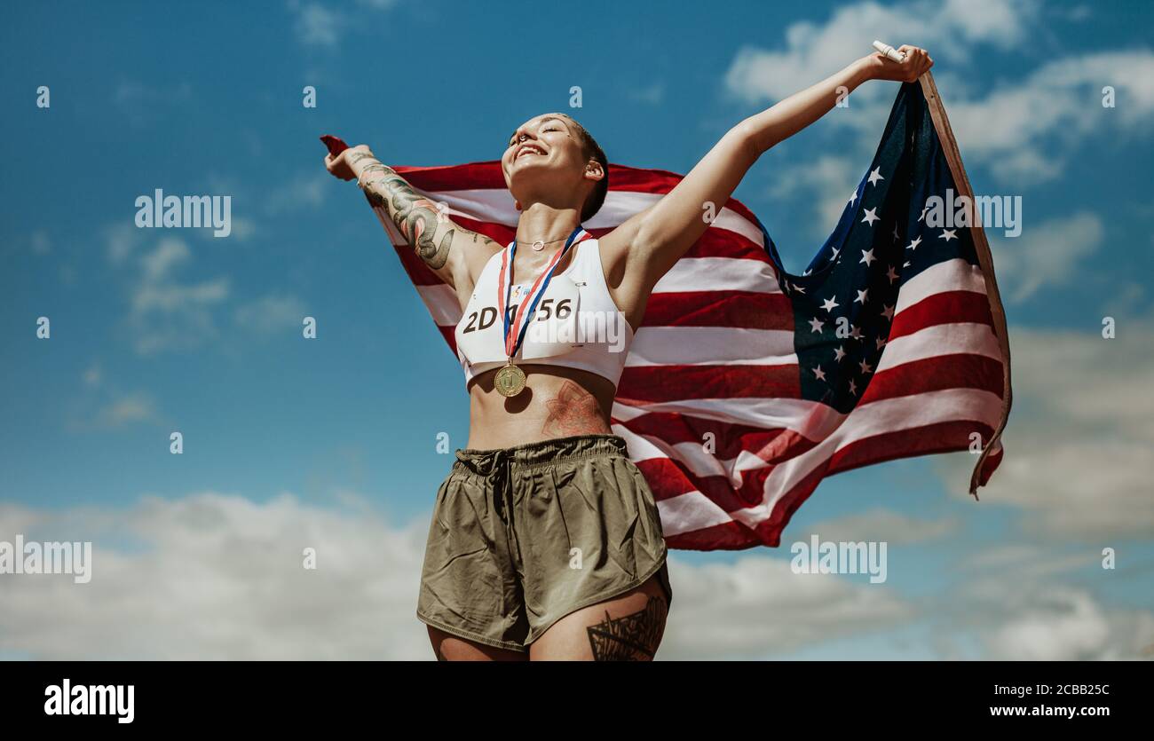 Athlet, der den Sieg mit US-Nationalflagge gegen Himmel genießt. Läuferin mit Medaillen, die einen Sieg mit amerikanischer Flagge feiern. Stockfoto