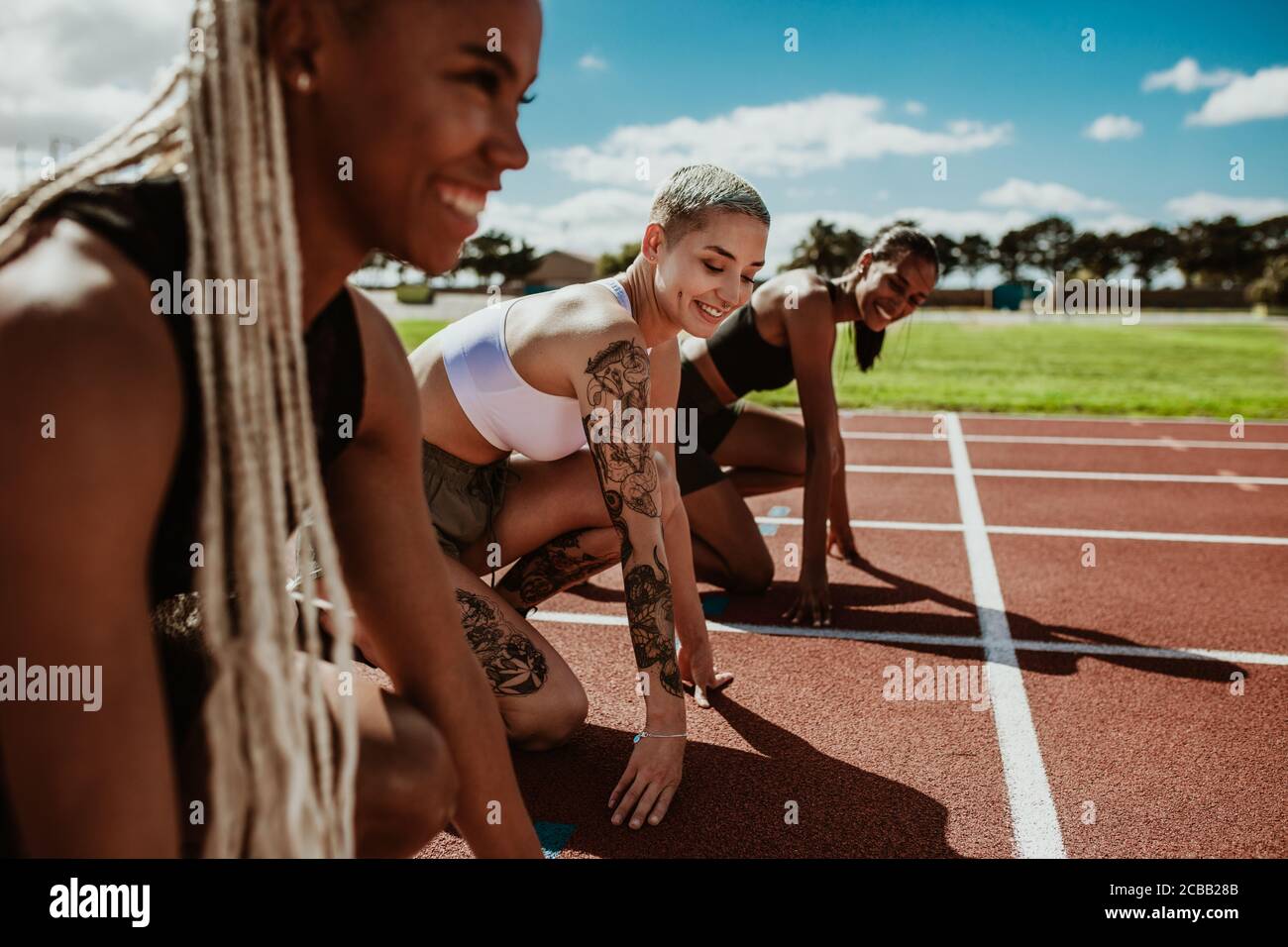 Drei weibliche Athleten an der Startposition bereit, ein Rennen zu starten. Sprinter bereit für das Rennen auf der Rennstrecke. Stockfoto