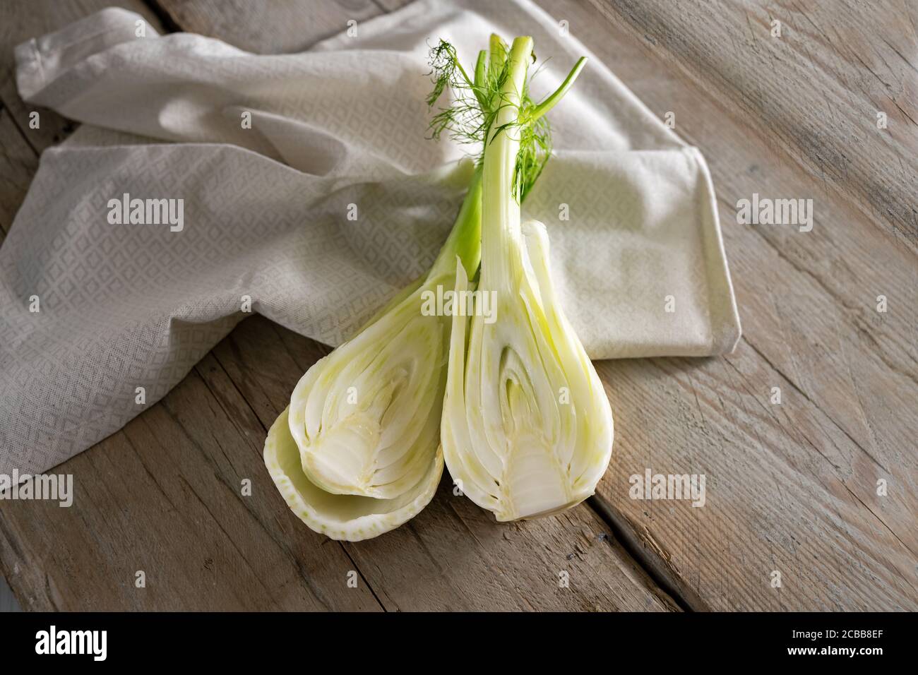 Frische rohe Fenchelknolle halbiert, gesundes Gemüse zum Kochen eines mediterranen Sommergerichtes auf Serviette und rustikalen Holzplanken, Kopierraum, ausgewählter Fokus, Stockfoto