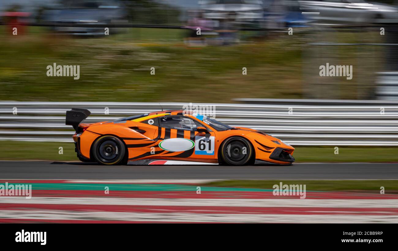Eine Schwenkaufnahme eines orangefarbenen Rennwagens, der eine Strecke fährt. Stockfoto