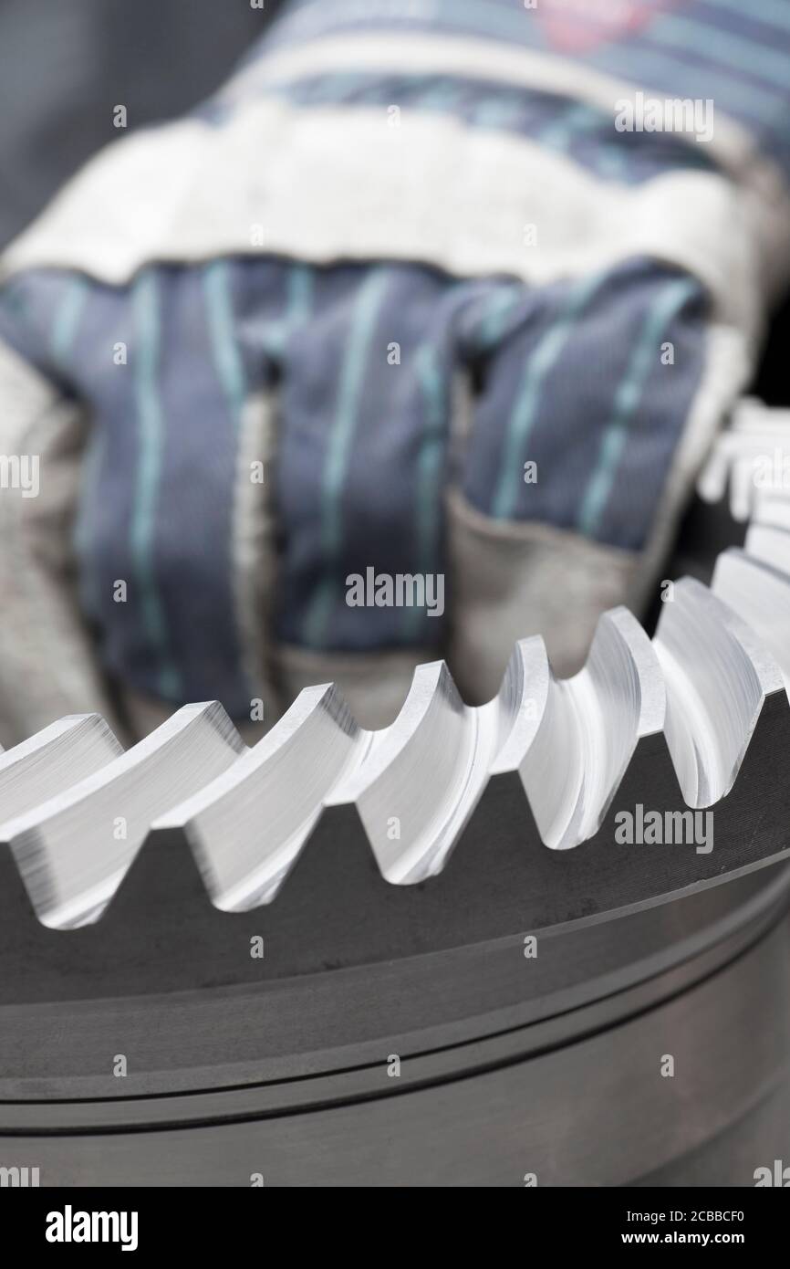 Die Hand des Mechanikers mit dem Arbeitshandschuh, der einen großen trägt Zahnrad - selektiver Fokus auf den Vordergrund Stockfoto