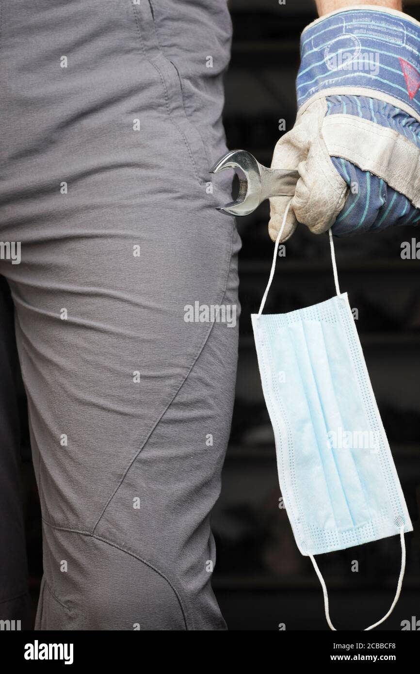 Mechaniker mit Arbeitshandschuhe tragen eine Gesichtsmaske und ein Schraubenschlüssel in der Hand - mit einer Werkstatt in der Hintergrund Stockfoto