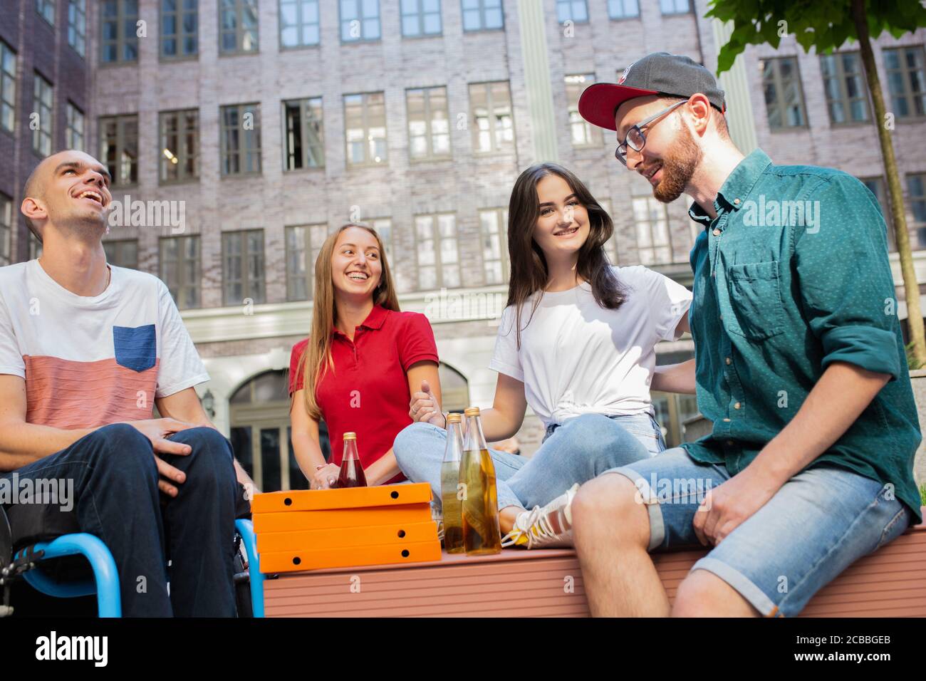 Pizza-Zeit. Eine Gruppe von Freunden, die am Sommertag auf der Straße der Stadt spazieren gehen. Behinderter Mann mit seinen Freunden, die Spaß haben. Inklusion und Diversity-Konzept, normale Lebensweise von besonderen Gruppen der Gesellschaft. Stockfoto