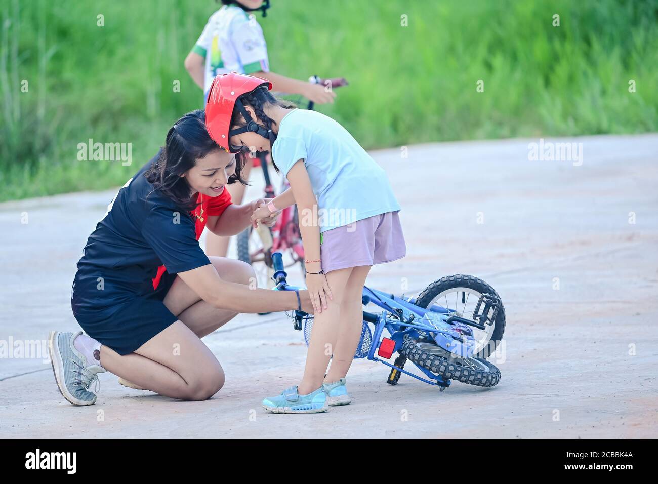 Mutter hilft ihrer kleinen Tochter, nachdem sie vom Fahrrad im Freien Kind mit Fahrradhelm fallen. Sicherheit Sport Freizeit mit Kindern Konzept Stockfoto