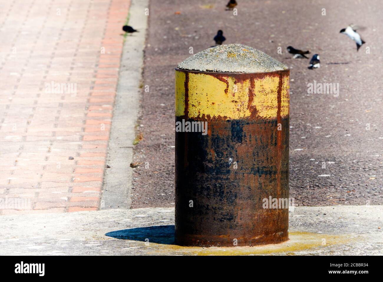Rostiger Poller mit gelber Farbe oben auf dem Betonboden der Anlegestelle im Hafen Stockfoto