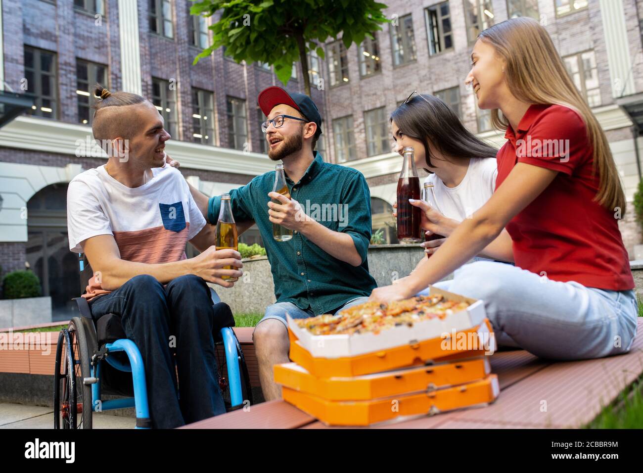 Pizza-Zeit. Eine Gruppe von Freunden, die am Sommertag auf der Straße der Stadt spazieren gehen. Behinderter Mann mit seinen Freunden, die Spaß haben. Inklusion und Diversity-Konzept, normale Lebensweise von besonderen Gruppen der Gesellschaft. Stockfoto
