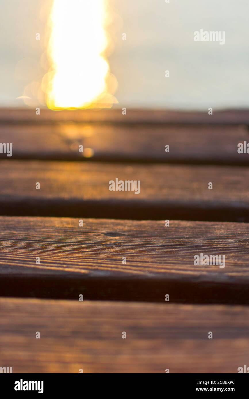 Holzdeck einer Anlegestelle am Gardasee. Die Sonne spiegelt sich im Wasser. Das Holz ist warm, braun gefärbt. Stockfoto