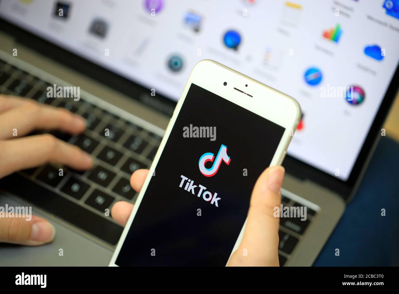 Eine Hand, die ein iPhone mit dem Logo von Online hält Video-Sharing und Hosting-App Tik Tok auf dem Bildschirm Vor einem Computer Stockfoto