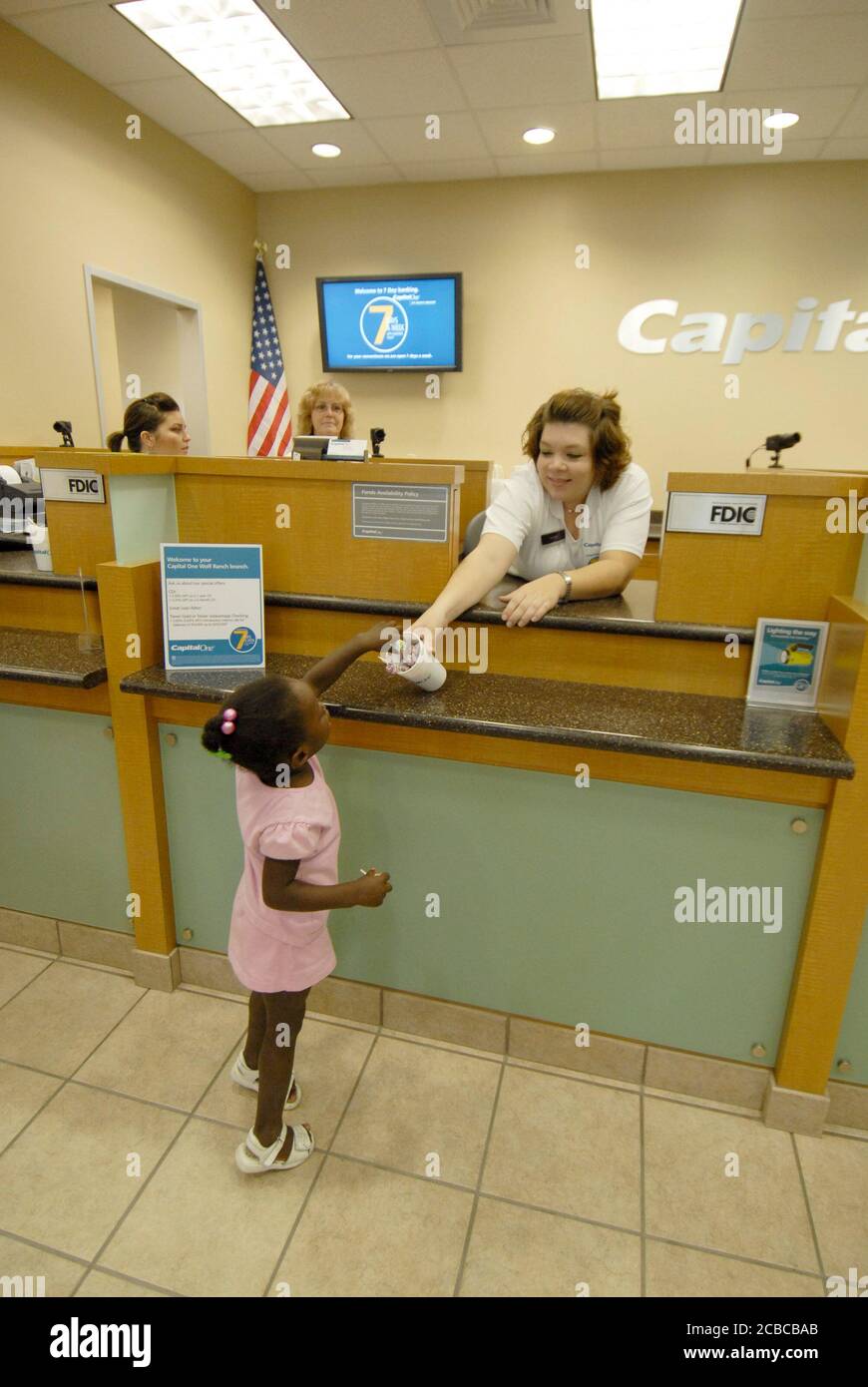 Georgetown, Texas, USA, 1. August 2006: Öffentliche Eröffnungsveranstaltung für eine Bank eines Capital One Bankzentrums im Williamson County nördlich von Austin in einem wachsenden Vorstadtgebiet. Ein afroamerikanisches Mädchen bekommt ein Stück Süßigkeiten vom Kassierer bei der großen Eröffnung. ©Bob Daemmrich Stockfoto