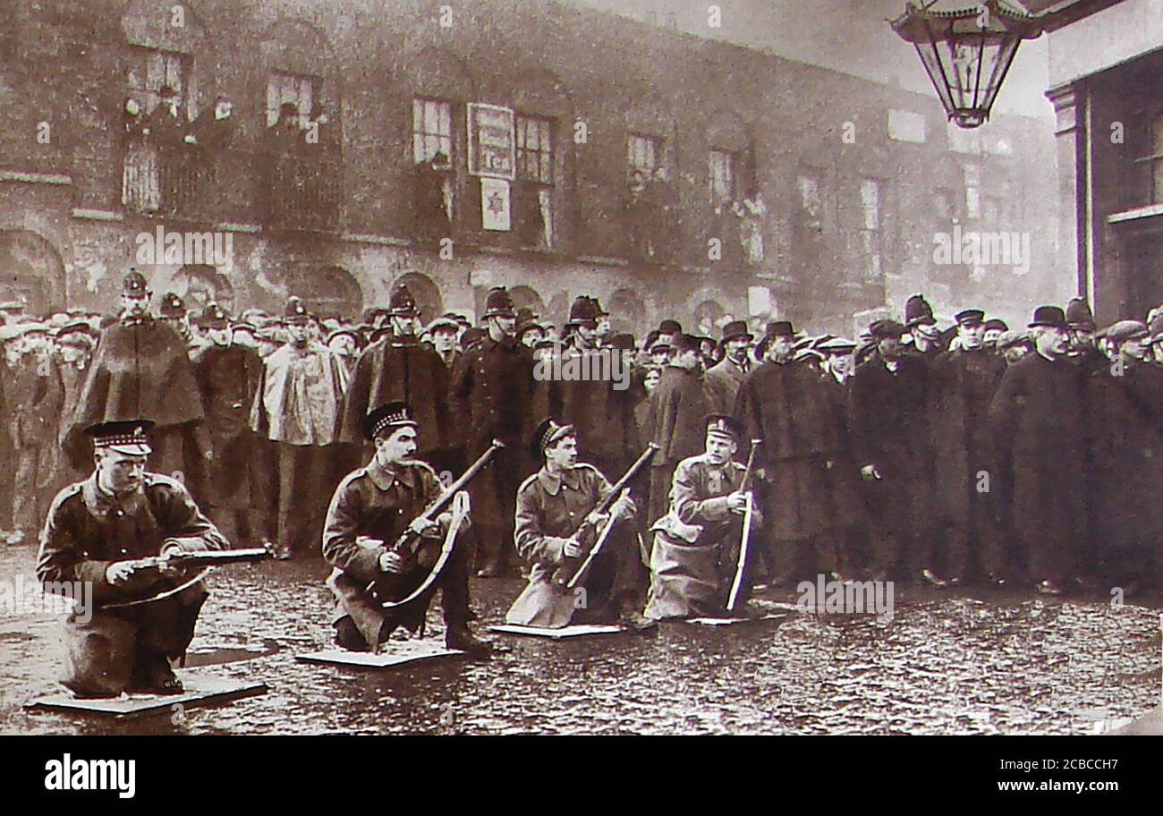 Seige of Sidney Street - die Belagerung der Sidney Street (Januar 1911), auch bekannt als die Schlacht von Stepney, nahm am East End von London zwischen der britischen Polizei von Soldaten unterstützt, nach einem Raub und der Ermordung von drei Polizisten durch lettische revolutionäre. Dieses historische Foto zeigt Soldaten, die ihre Gewehre mit Massen von Zuschauern beladen, die von britischen Polizisten ("Bobbies") zurückgehalten werden. Stockfoto