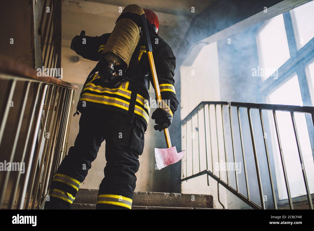 Junge Feuerwehrmann in Aktion, stehen in der Landung, gehen mit Feuer zu kämpfen, tragen Uniform und hält Hammer Stockfoto