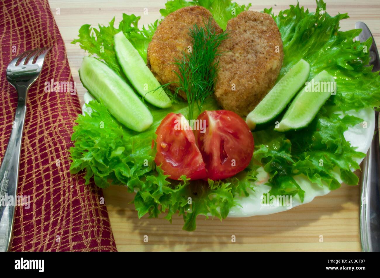 Portion Kartoffelschnitzel auf einem Teller mit Gemüse (Gurke, Tomaten) und Gemüse (Salat, Dill) Stockfoto