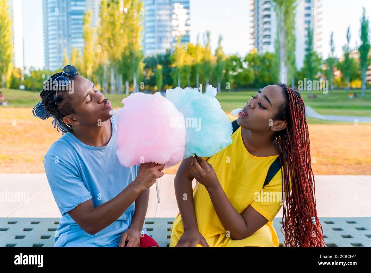 Ein glückliches schwarzes Paar, das bunte Zuckerwatte zusammen in einem Park einer großen Stadt hat. Stockfoto