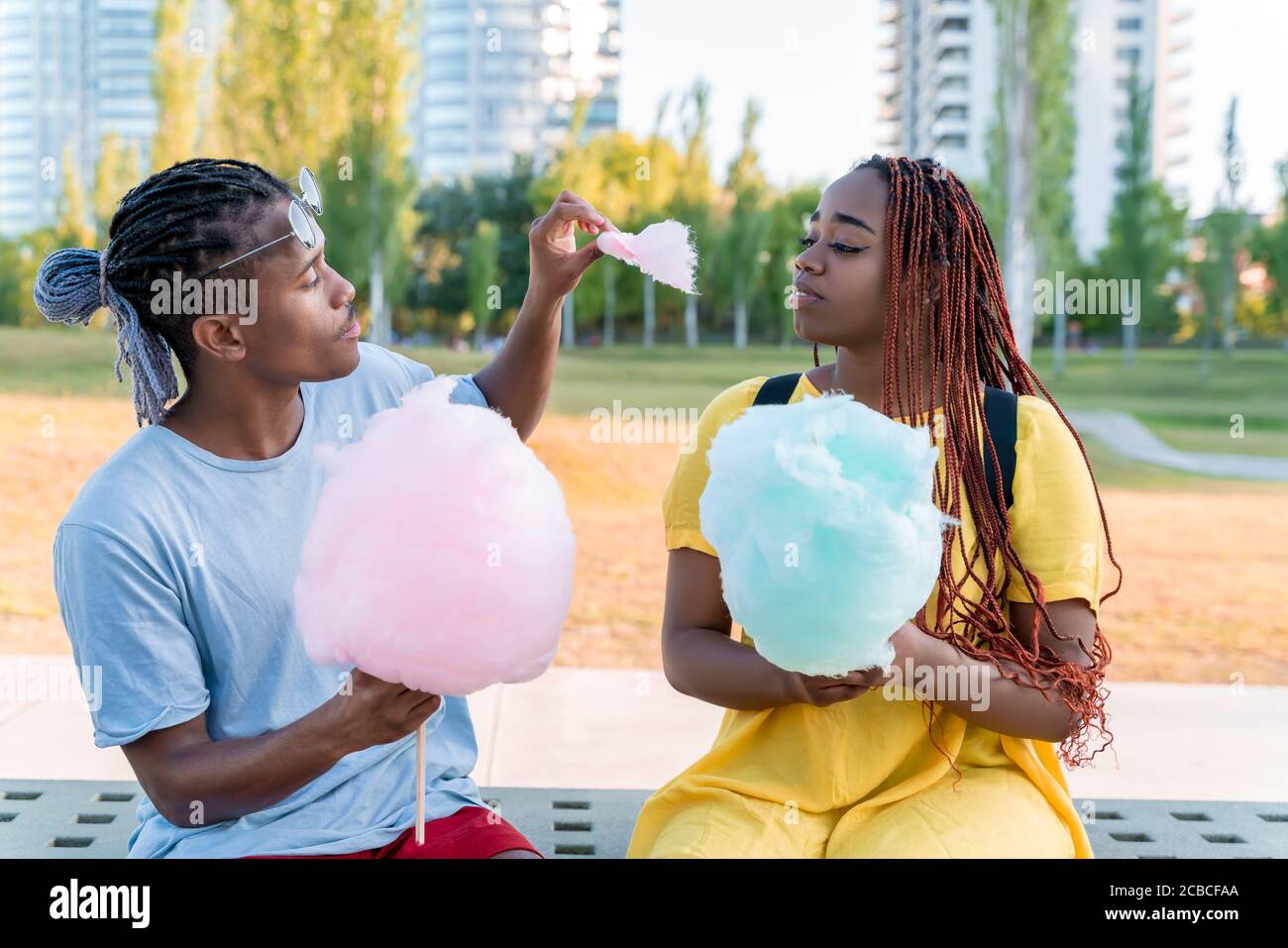 Ein glückliches schwarzes Paar, das bunte Zuckerwatte zusammen in einem Park einer großen Stadt hat. Stockfoto