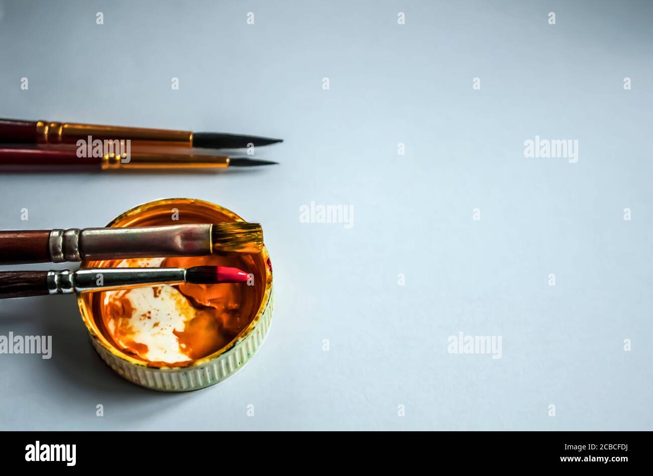 Gelbe Gouachekappe und vier Pinsel auf hellem Hintergrund Mit Platz für Text Stockfoto