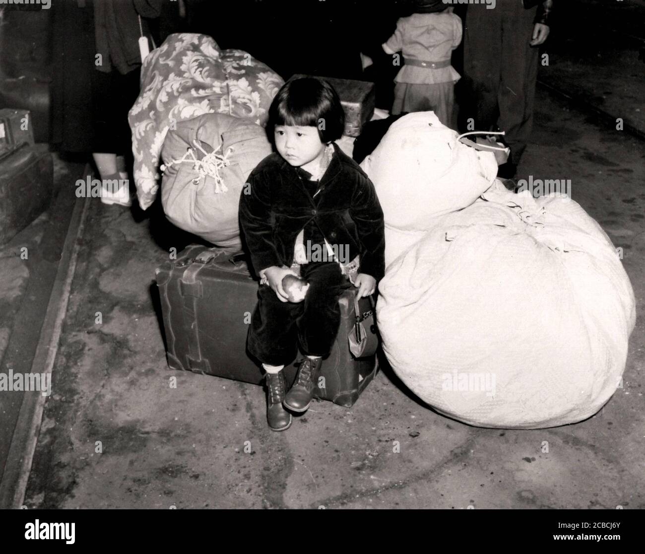 Ein junger japanischer Evakuierte wartet mit dem Familiengepäck, bevor er 1942 mit dem Bus zu einem Versammlungszentrum fährt. Kalifornien, 1942 Foto von Clem Albers (WRA) Stockfoto