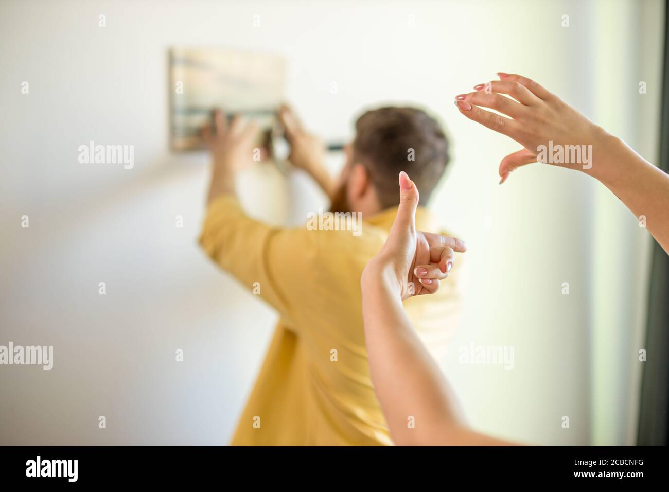 Nahaufnahme von weiblichen Händen während der Dekoration neue Wohnung, Mann hängen Bild an der Wand im Hintergrund Stockfoto