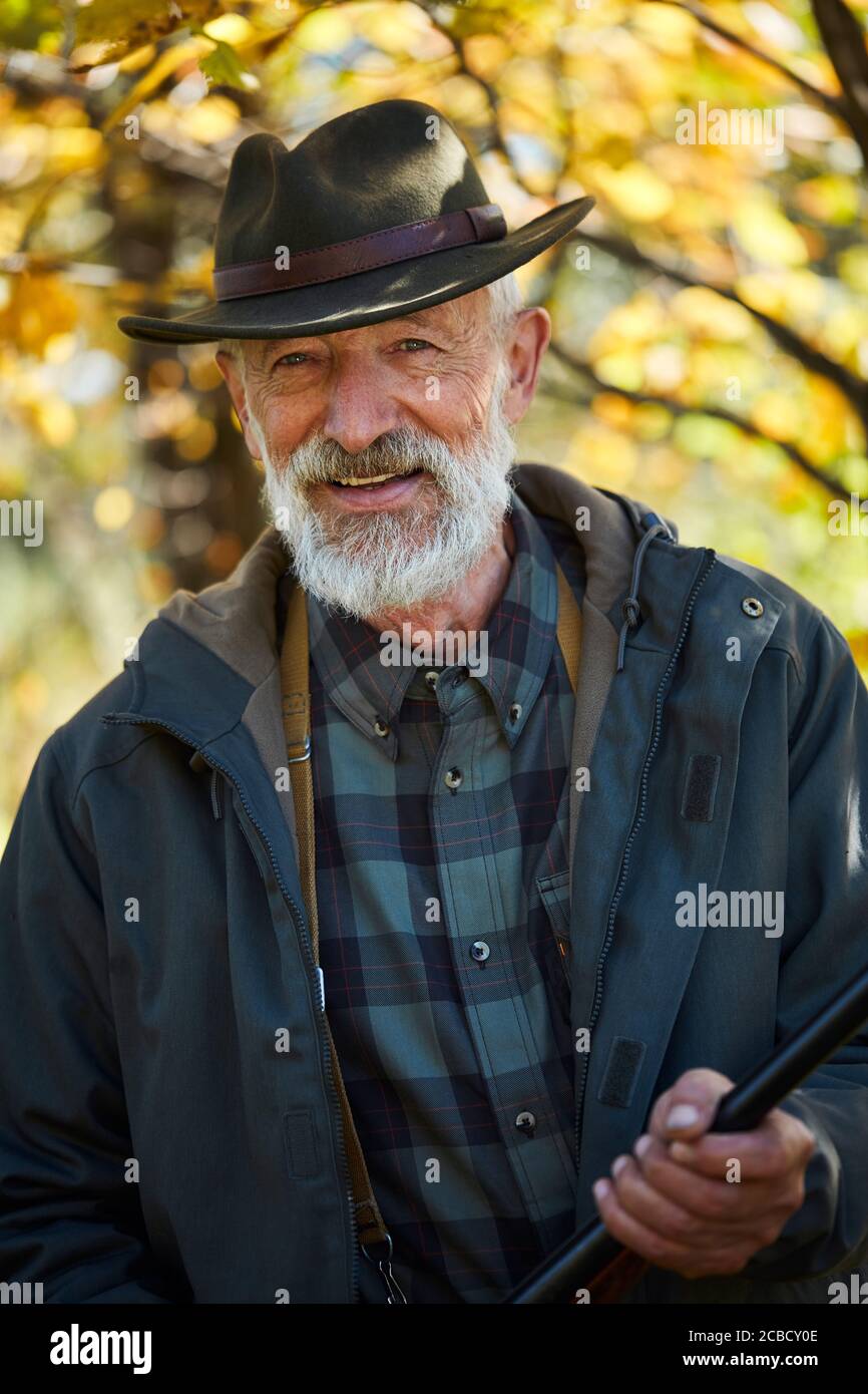 Reifer bärtiger Mann mit Waffe, lächelnd, glücklicher Jäger, der die Kamera anschaut. Erfolgreiche Jagd Stockfoto