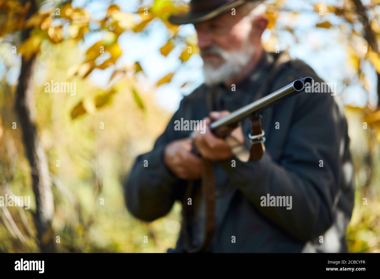 Beardy älterer Mann hält Gewehr im Wald. Nahaufnahme Stockfoto