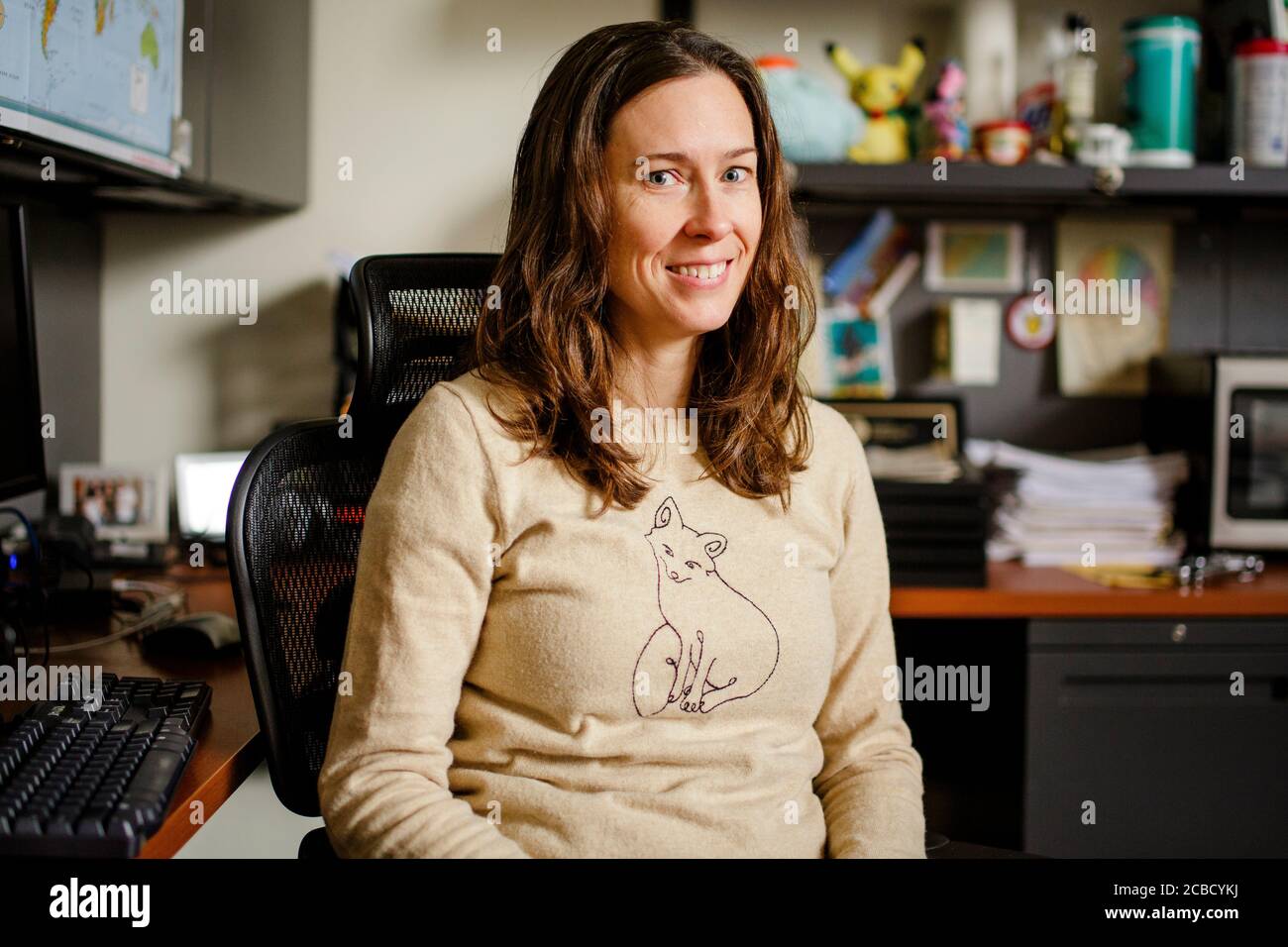 Eine Professorin sitzt lächelnd an ihrem Schreibtisch Direkter Blick Stockfoto