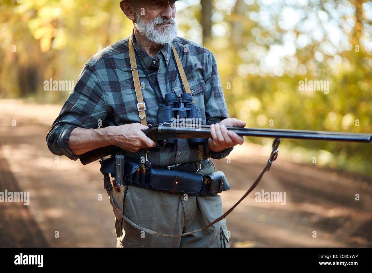 Älterer Jäger Mann mit grauem Bart halten Waffe auf Vögel jagen, bereit zu schießen. Waldhintergrund Stockfoto