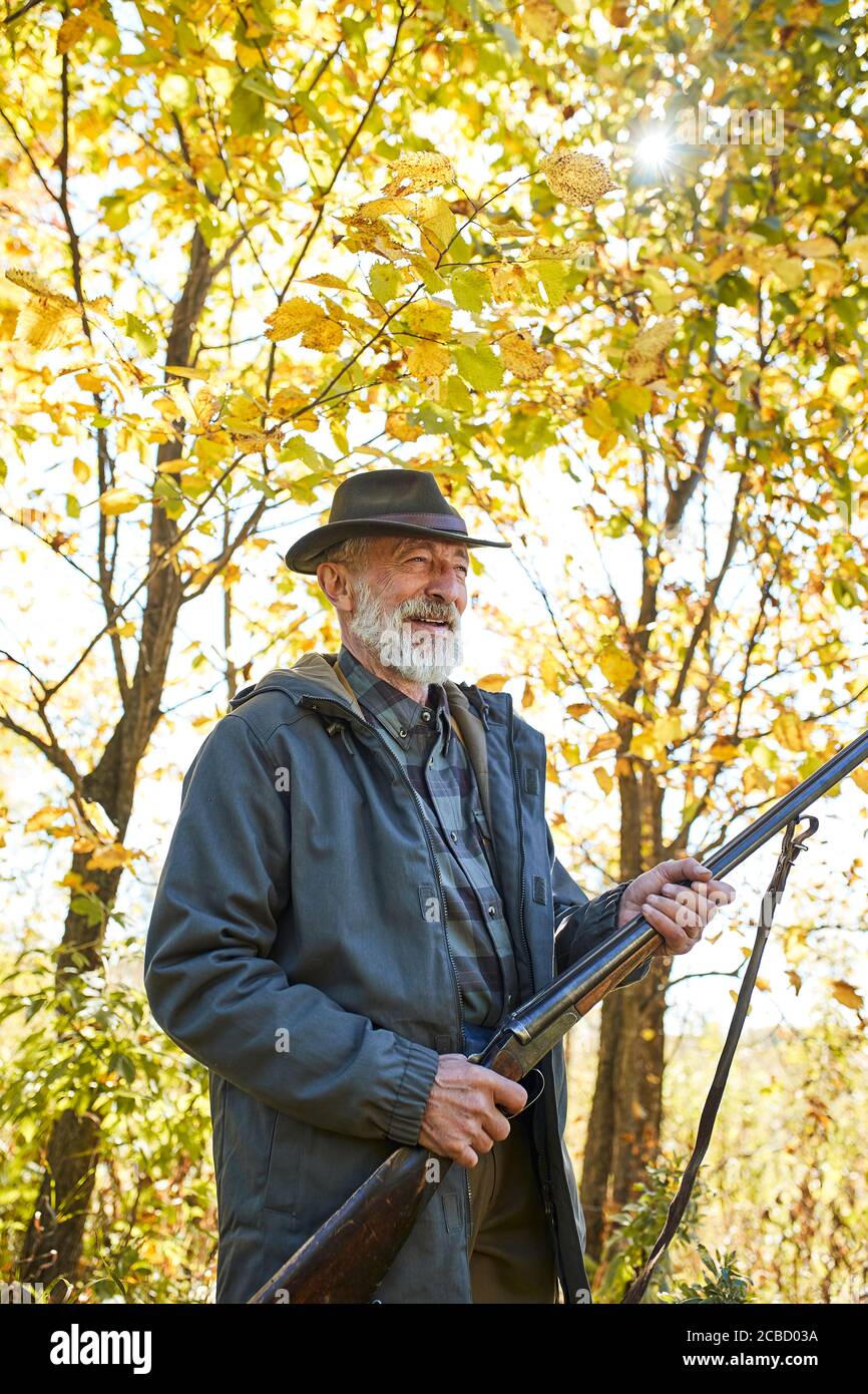 Lächelnder Jäger männlich stehen Waffe halten und wegschauen, tragen Hut und Mantel, Herbst Stockfoto