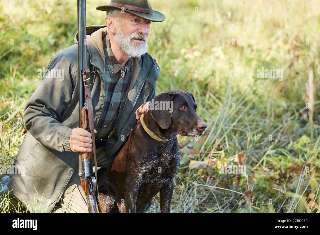 Kaukasischer reifer Mann mit Pistole und Hund sitzen auf der Suche Beute. Bärtiger Mann in Jagdkleidung. Herbst Stockfoto