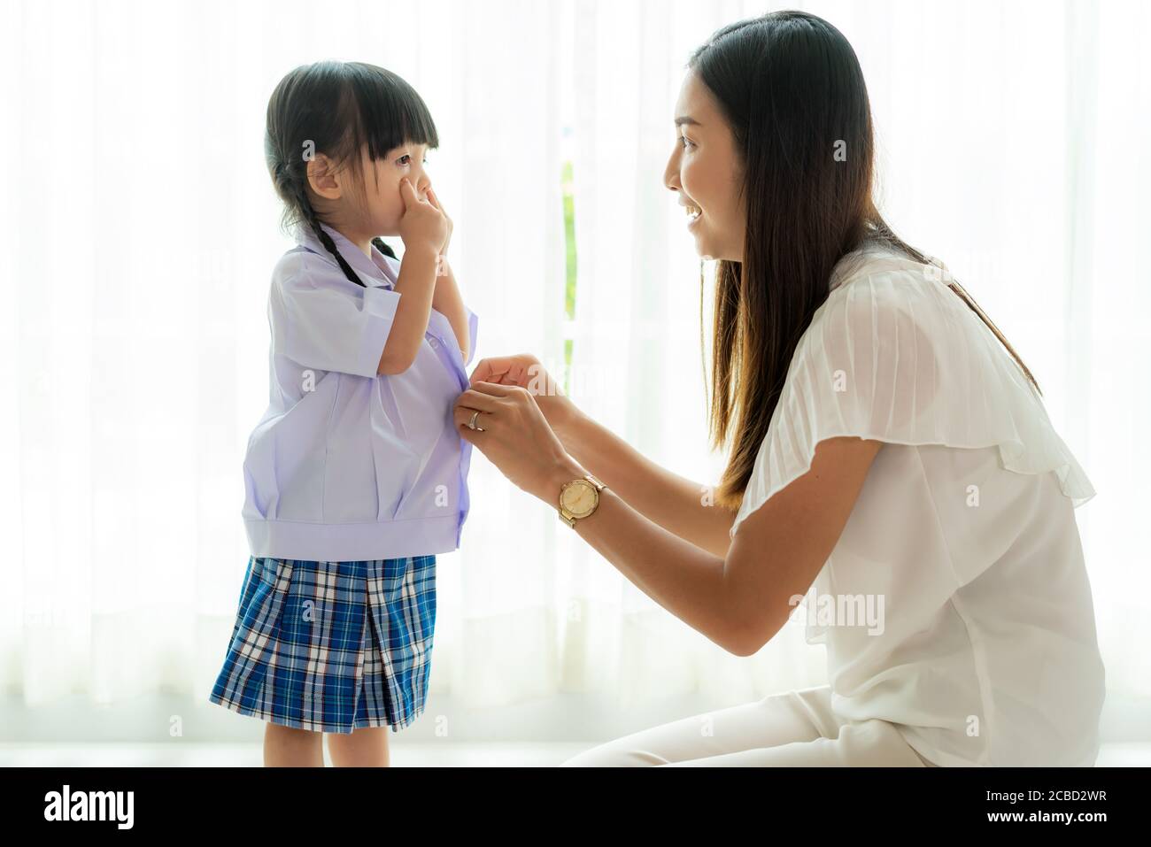 Asiatische Mutter Vorbereitung Kindergarten Schüler Uniform zu ihrem kleinen Tochter für die Schule immer bereit für die Schule im Wohnzimmer zu Hause. Elternschaft oder l Stockfoto