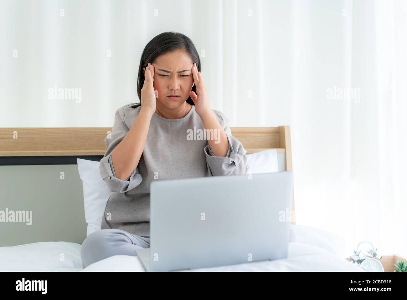 Asiatische Frau im weißen Bett sprechen mit Arzt mit Tele Gesundheitstechnologie, während sie auf einem Sofa sitzen und Kopfschmerzen im Schlafzimmer zu Hause, während sie duri krank Stockfoto