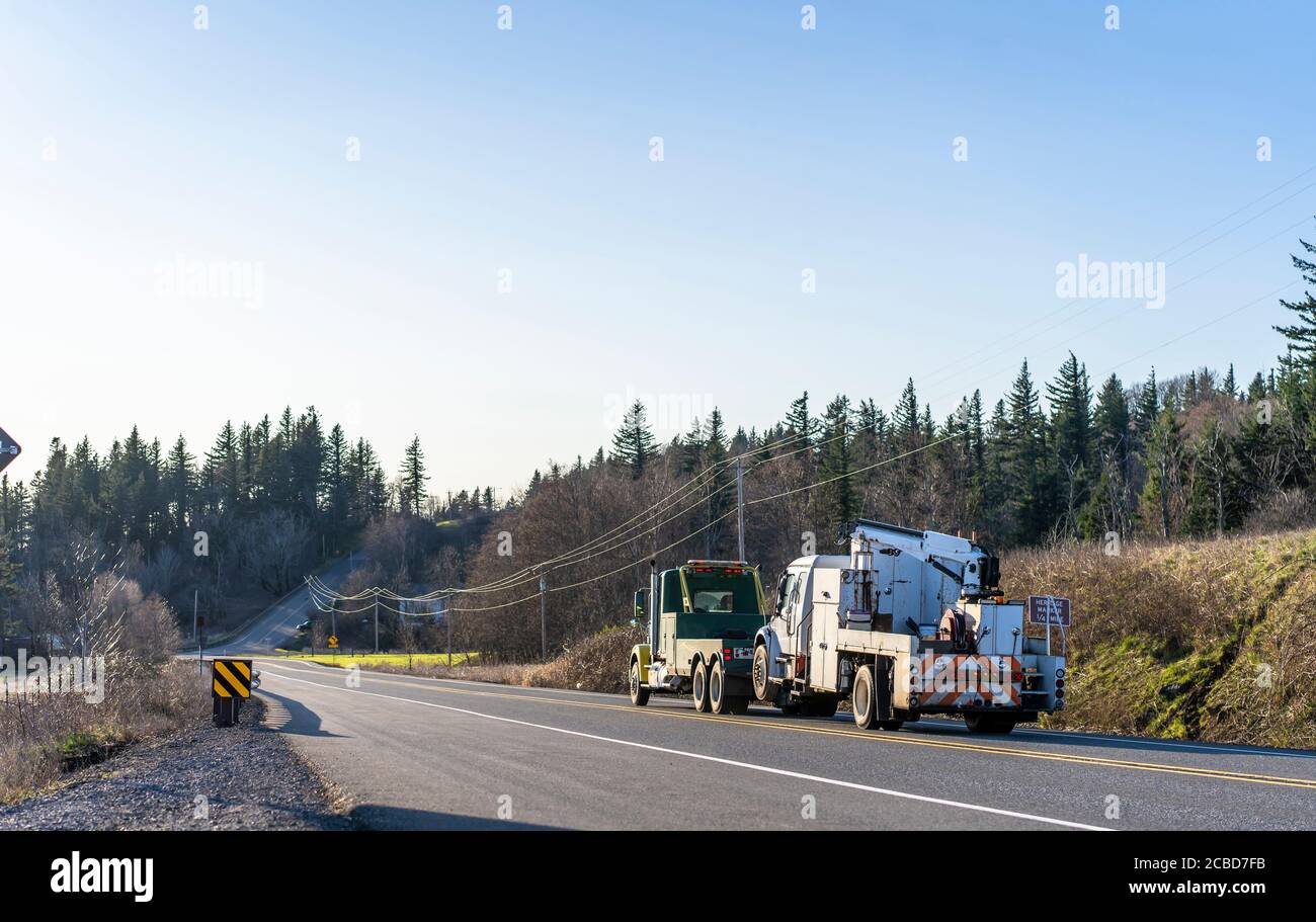 Big Rig Schwerlast Abschleppen semi-Truck Abschleppen eine andere gebrochen groß Rig Sattelschlepper mit Anwendung auf eine Werkstatt läuft Auf der Straße mit Hügel und Bäumen i Stockfoto