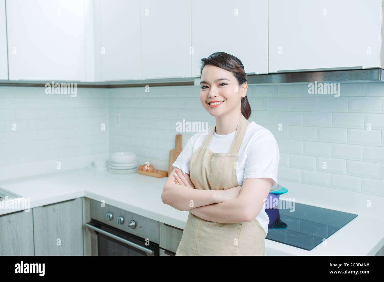 Porträt einer jungen Frau, die mit gekreuzten Armen vor Küchenhintergrund steht Stockfoto