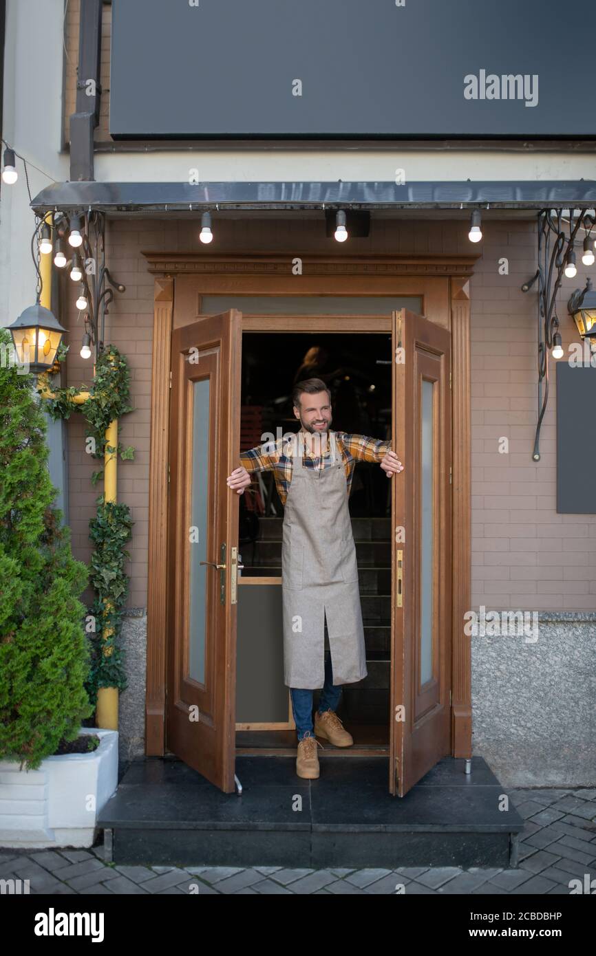 Bärtiger Mann im Vorfeld, der die Türen des Cafés öffnete und lächelte Stockfoto