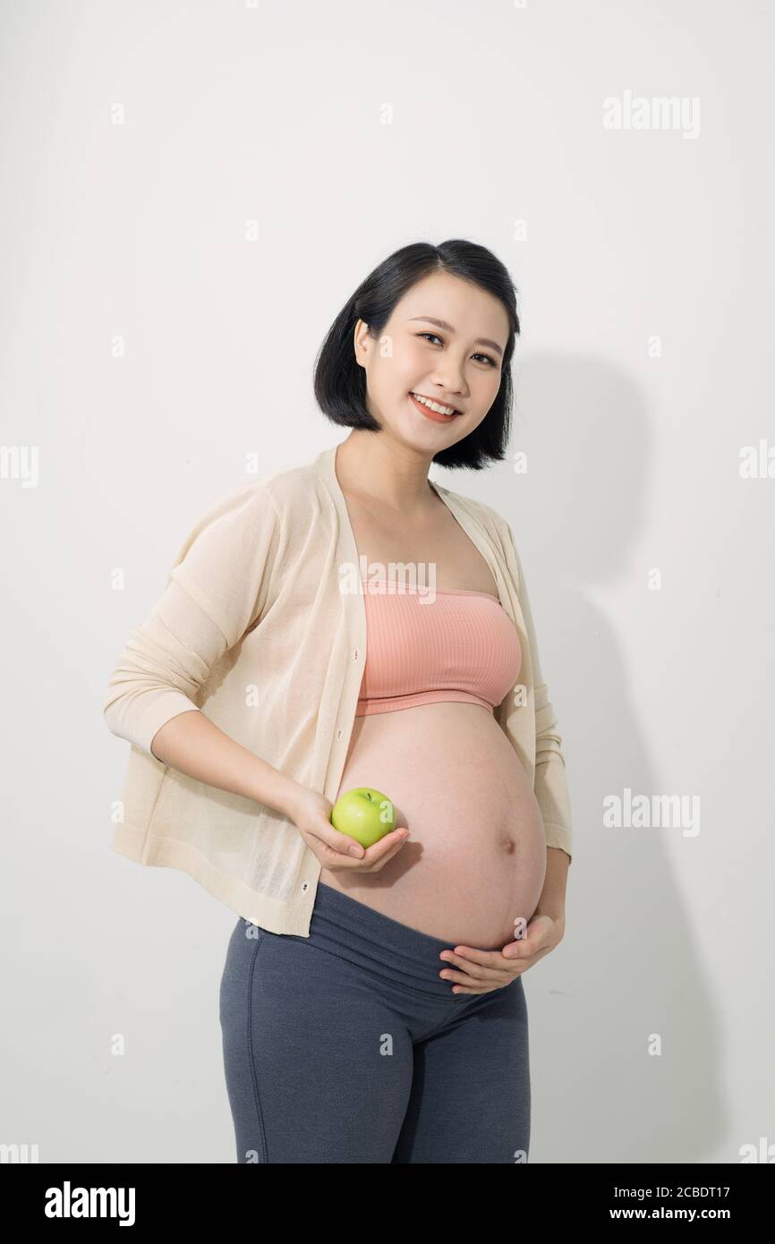 Nur einen Apfel am Tag. Schöne junge schwangere Frau mit Lächeln und hält grünen Apfel, während auf weißem Hintergrund stehen Stockfoto