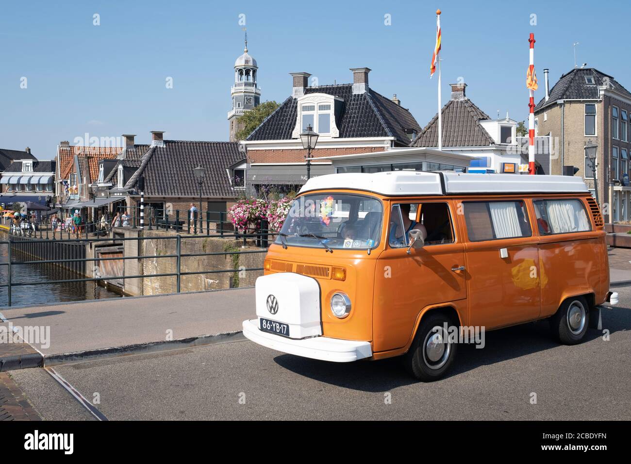Orange Retro Volkswagen Transporter mit weißem Dach und eingerichtet als Camper mit weißen Vorhängen fährt über den Blokjesbrug in Lemmer, Friesland Stockfoto